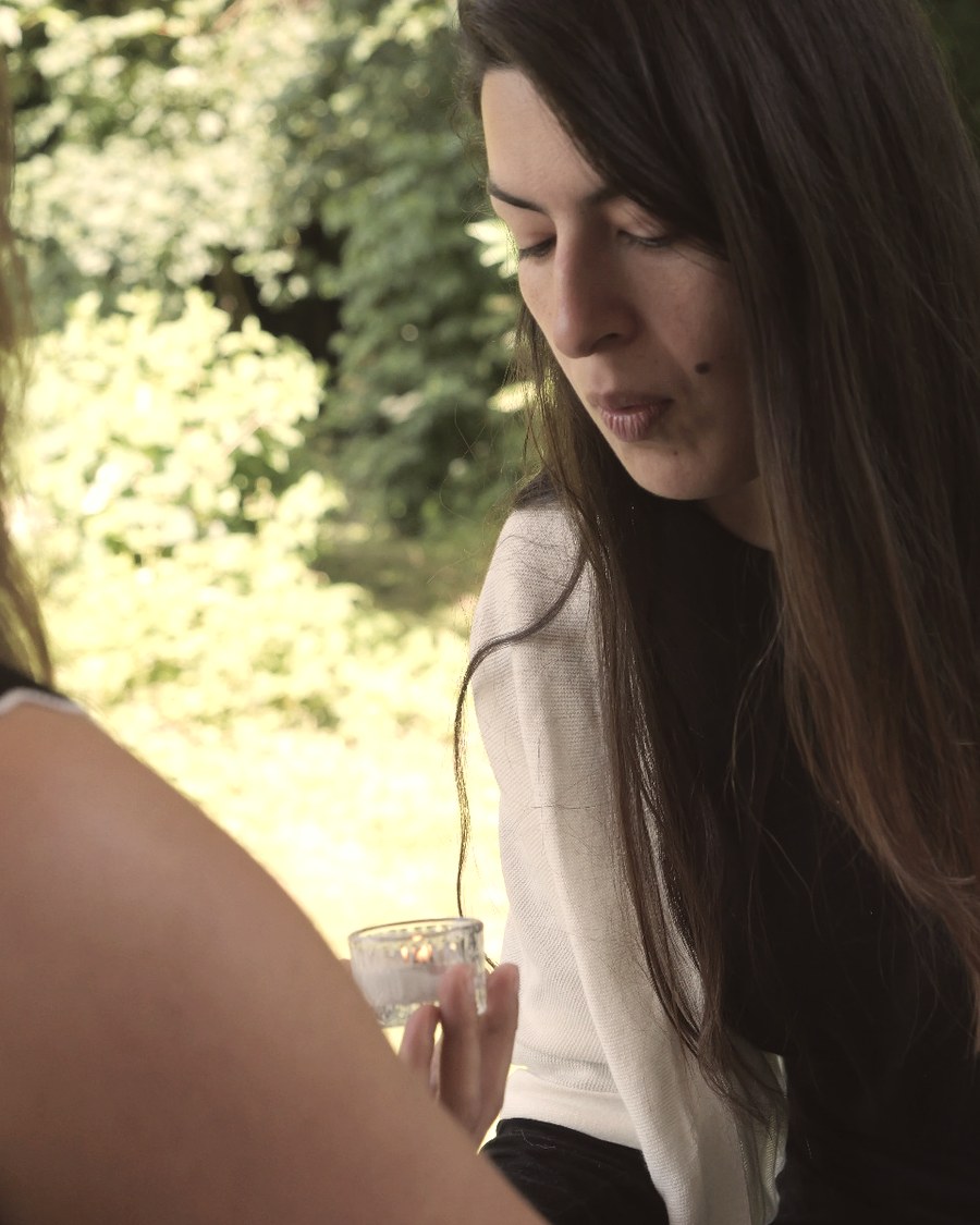 Deux femmes assises en extérieur, en conversation, un verre à la main